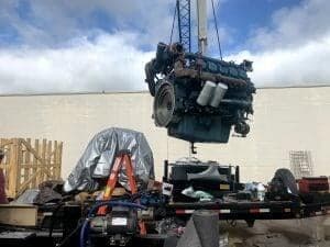 Crane lifting a diesel engine block onto a trailer during a generator rebuild