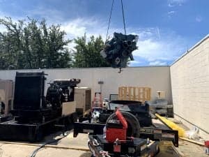 Crane lowering a diesel engine over a generator trailer in the Alturex shop yard